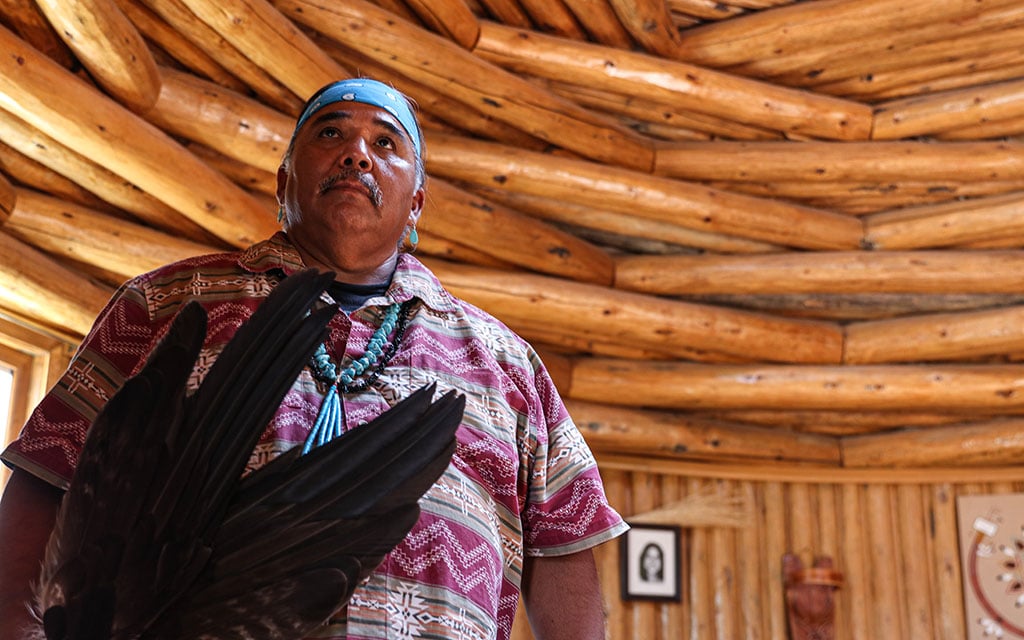 Wayne Wilson, standing in a hogan at the Native American Baha’i Institute in Houck, holds eagle feathers he uses in traditional healing ceremonies. © Laura Bargfeld/Cronkite News