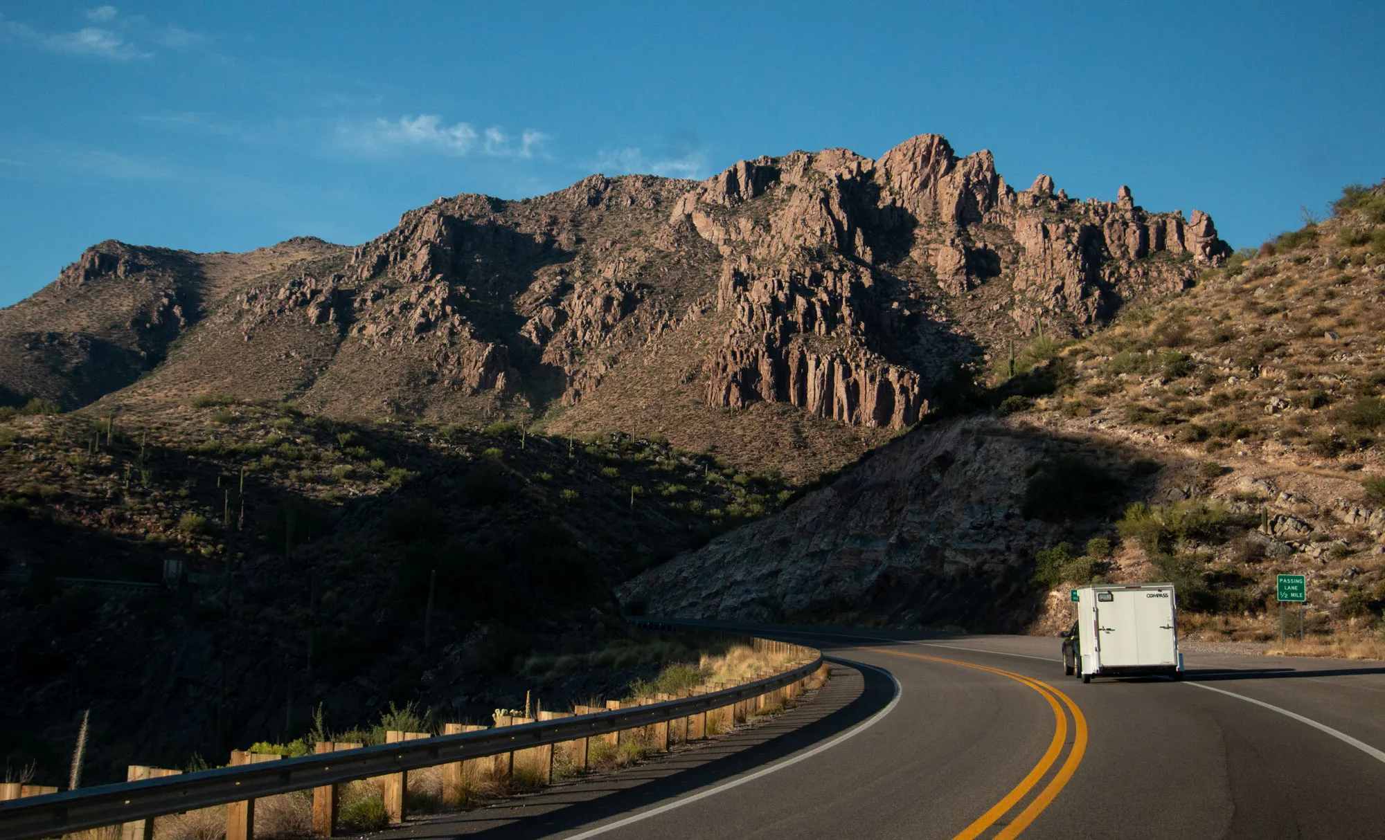 Vehicle and trailer driving on a curved Arizona road with mountains in the background.