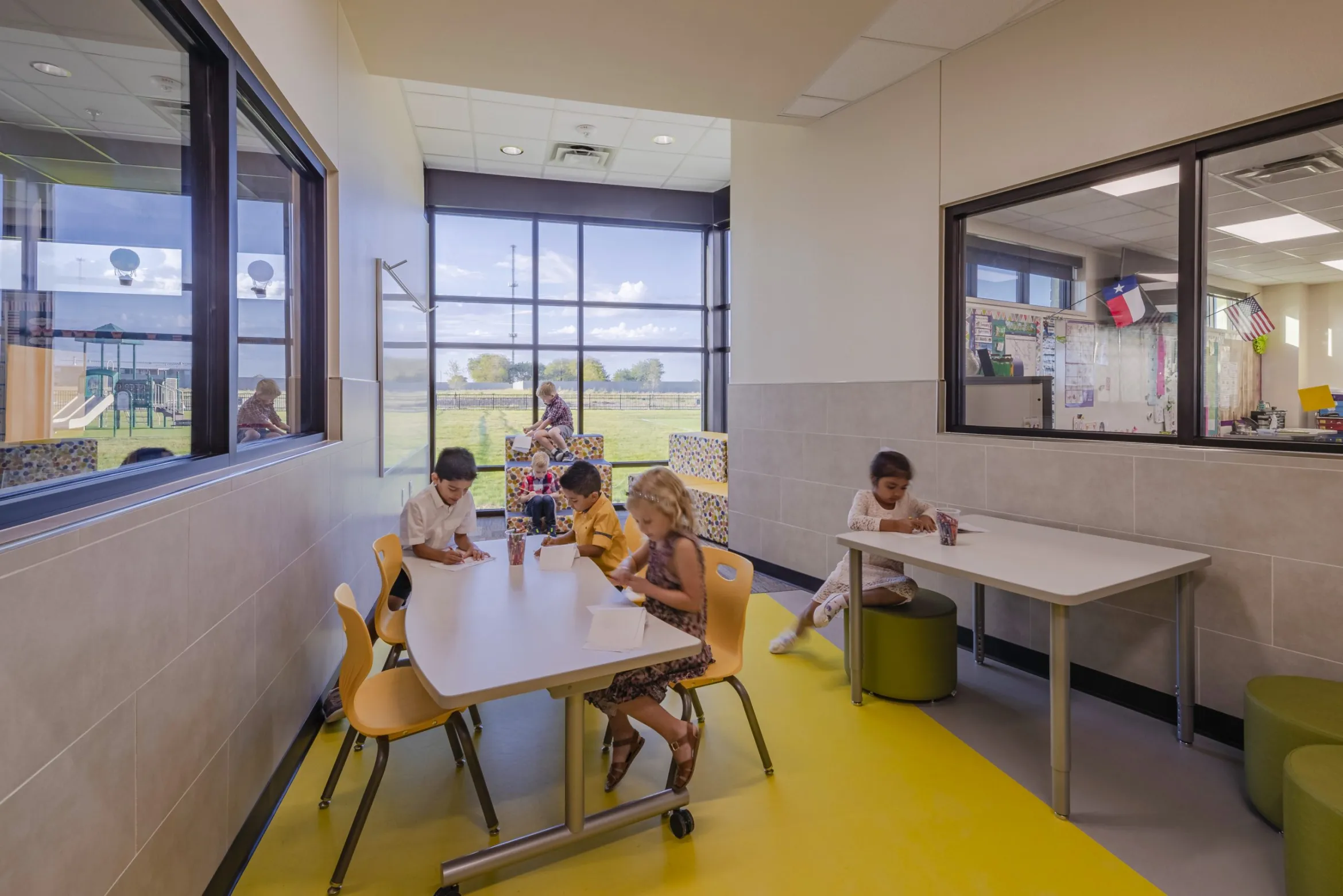 Six children sit together working individually in a colorful, collaborative workspace with a big window.