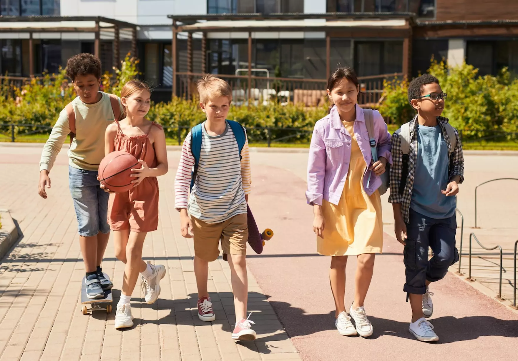 Five children walk together on a sunny day. They each have backpacks, probably leaving school.