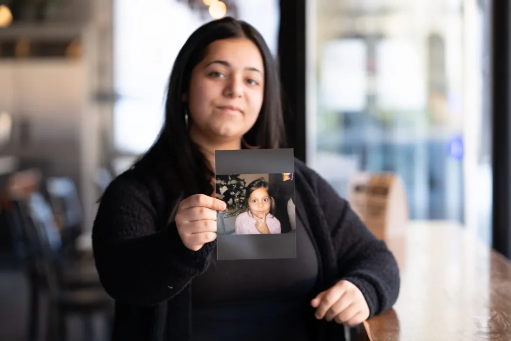 Olivia Frausto, now 19, holds a photo of her younger self, taken before she entered West Virginia’s child welfare system. Photo by Jenny Lynn Photography
