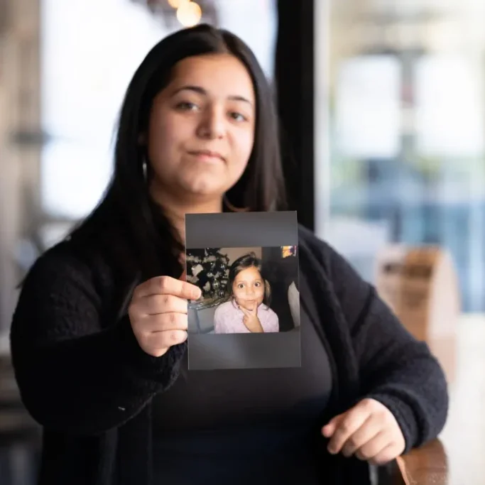 Olivia Frausto, now 19, holds a photo of her younger self, taken before she entered West Virginia’s child welfare system. Photo by Jenny Lynn Photography
