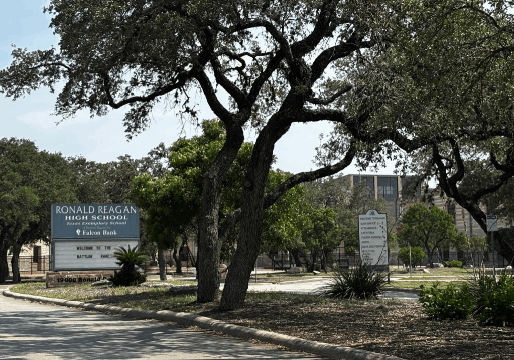A sign that reads Ronald Reagan High Schools sits in front of a building.