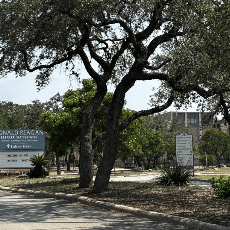 A sign that reads Ronald Reagan High Schools sits in front of a building.