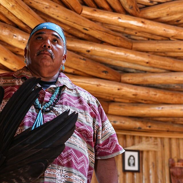 Wayne Wilson, standing in a hogan at the Native American Baha’i Institute in Houck, holds eagle feathers he uses in traditional healing ceremonies. © Laura Bargfeld/Cronkite News