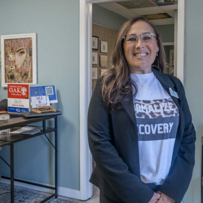 ©Sofi Gratas/GPB: Jocelyn Wallace, executive director of The Never Alone Clubhouse, stands at the entrance of the recovery center in Douglas County. As someone in recovery herself, she opened this place two years ago to give people who have dealt with substance use disorder a chance to connect.