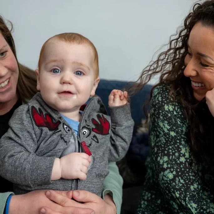 Cam (center) held by his mother, Jen Shea (left), tugs on the hair of doula Desirae Whittle (right). The two have formed an enduring bond through Shea's two pregnancies and their shared struggles with postpartum depression.